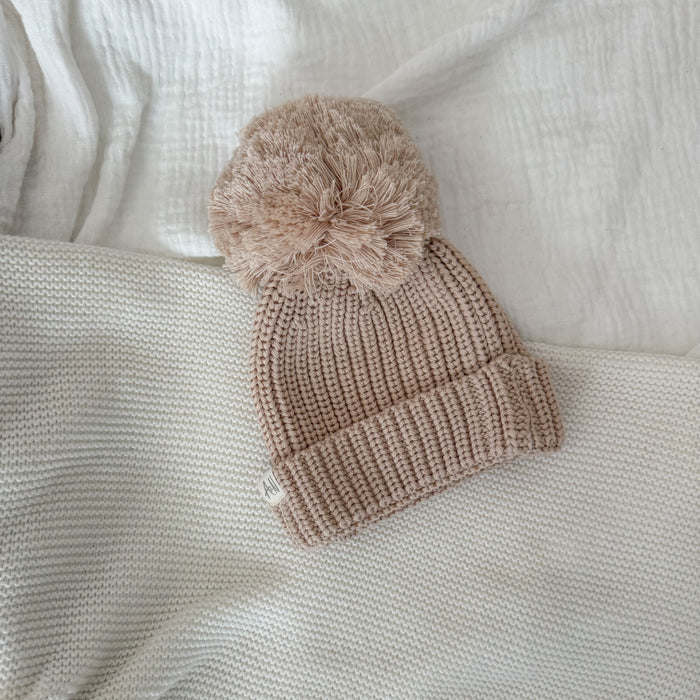 Beige knitted baby beanie with large pom-pom and ribbed brim