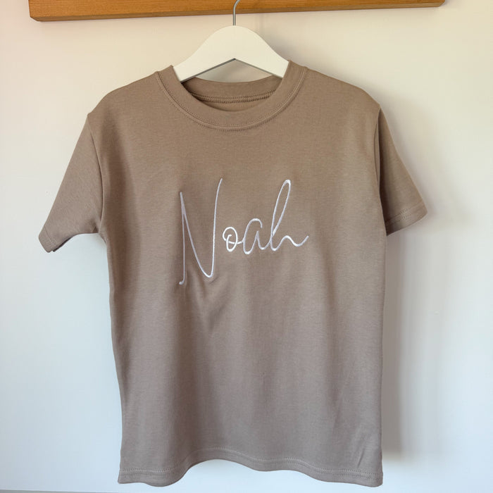 Taupe short-sleeve T-shirt with white cursive name print on the chest