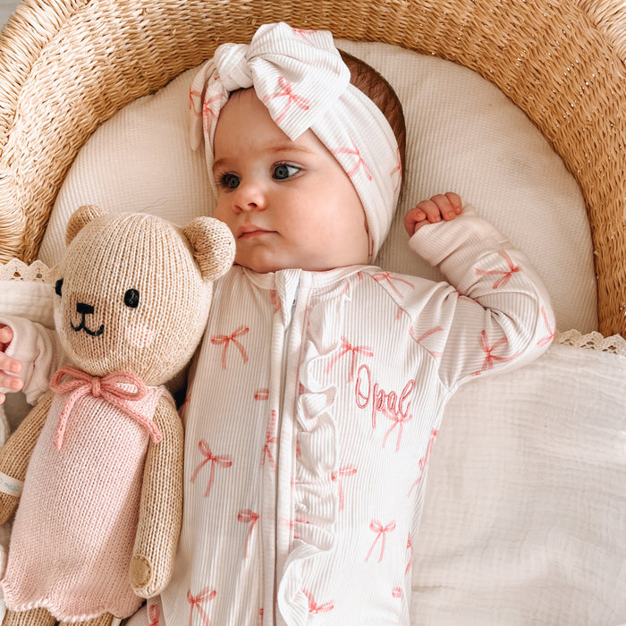 White ribbed zip sleepsuit with pink bow pattern and 'Opal' chest print, baby wearing