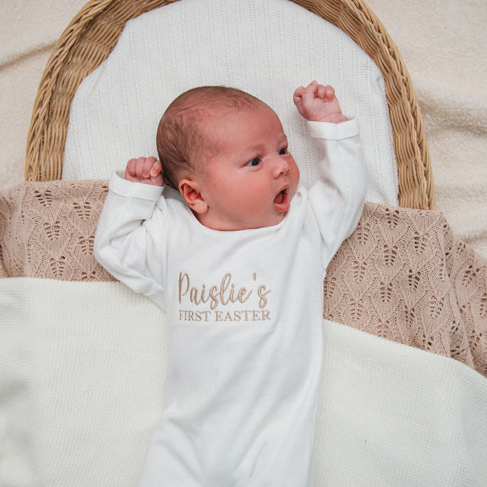 Baby wearing personalised first Easter sleepsuit in white, sleeves with 'Paislie's First Easter'