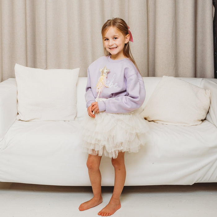 Lavender crewneck sweatshirt with white script embroidery, tulle skirt, holding star wand