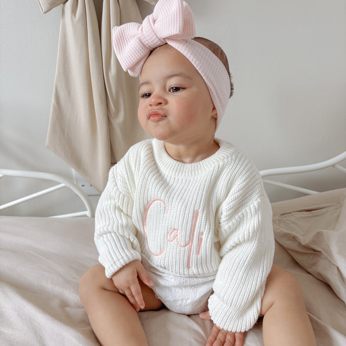 White knitted baby jumper with pink script detail, textured knit and ribbed cuffs
