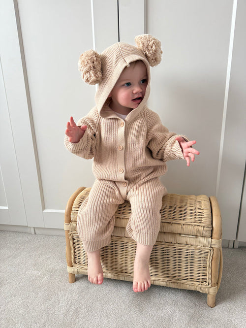 Beige hooded knit romper with pom-pom hat, long sleeves and button front