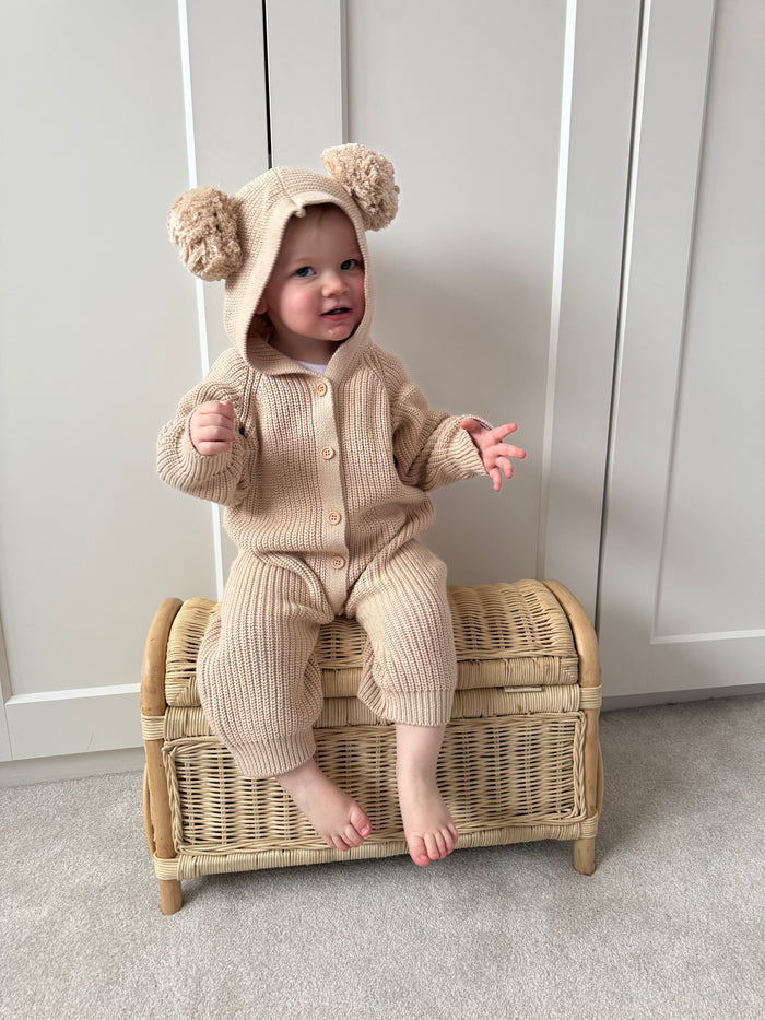 Beige hooded knit romper with pom-pom hat, long sleeves, button front, footed legs