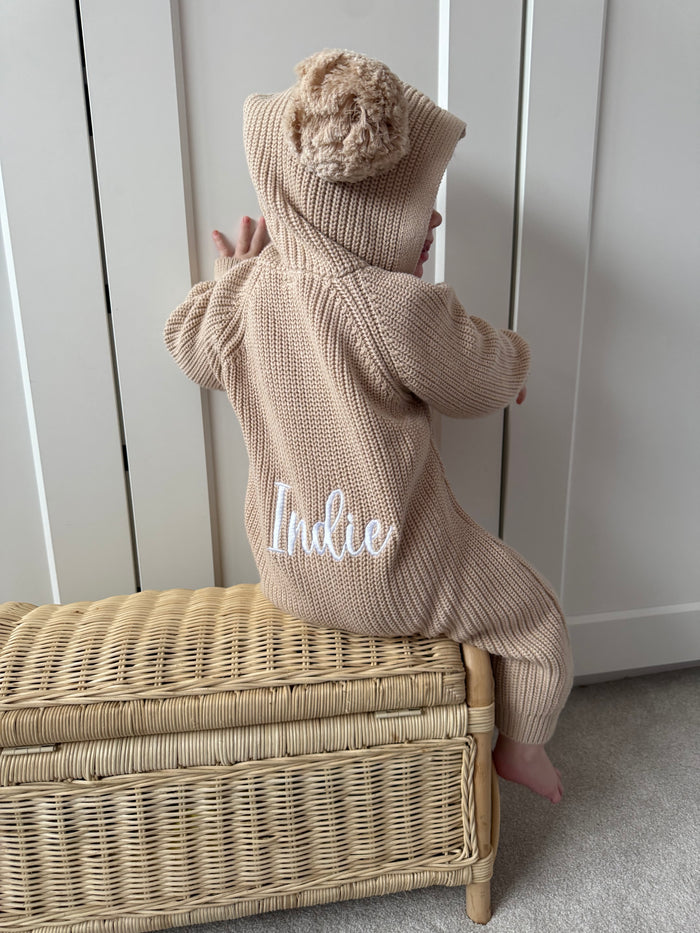 Beige hooded knit romper with pom-pom hood; back shows name "Little"