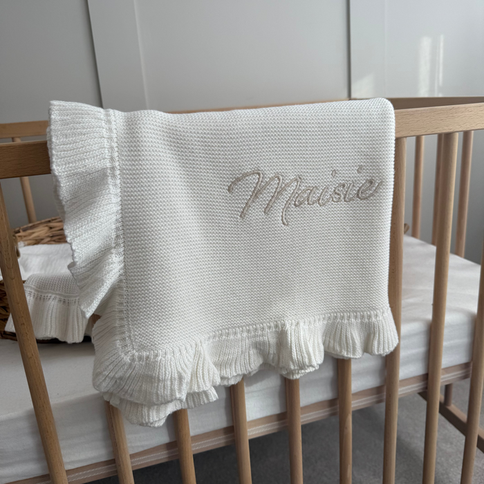 White knitted baby blanket with scalloped frill border and script embroidery