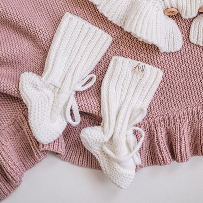 Pair of white knitted baby booties with ribbed cuffs and lace ties