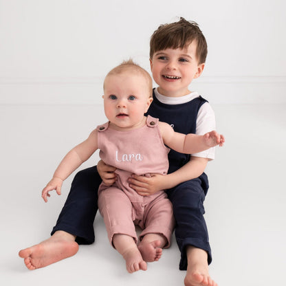 Dusty pink baby embroidered name dungarees with 'Lara' chest embroidery on seated baby