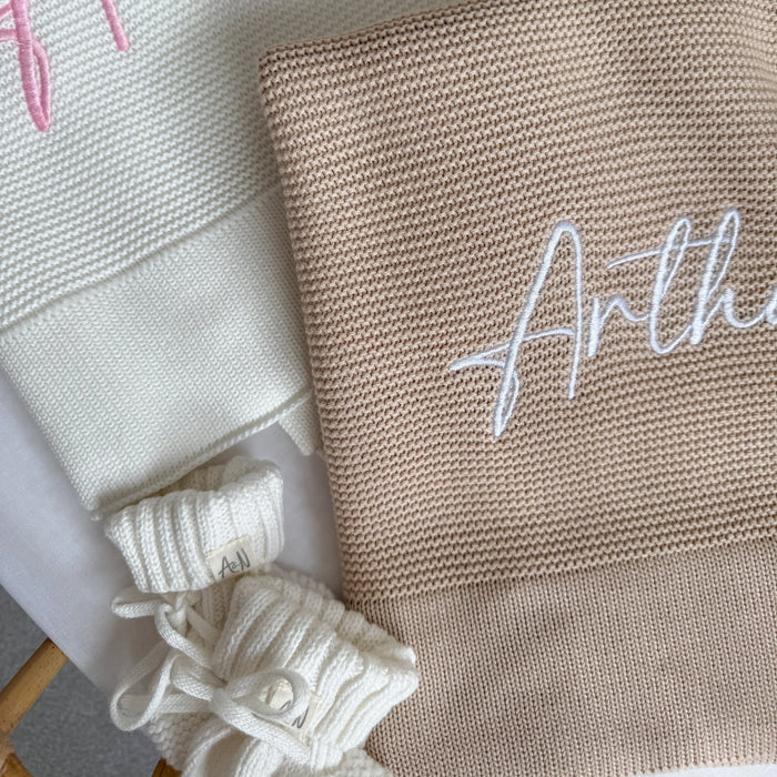Beige knit blanket corner with embroidered name 'Arthu' and white tied decorative trim