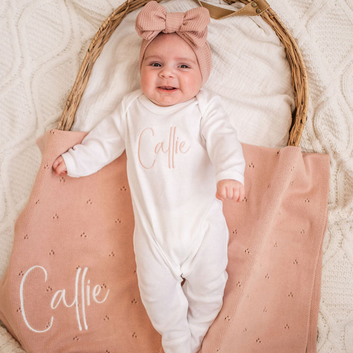 White long-sleeve baby sleepsuit with script 'Caitie' on front