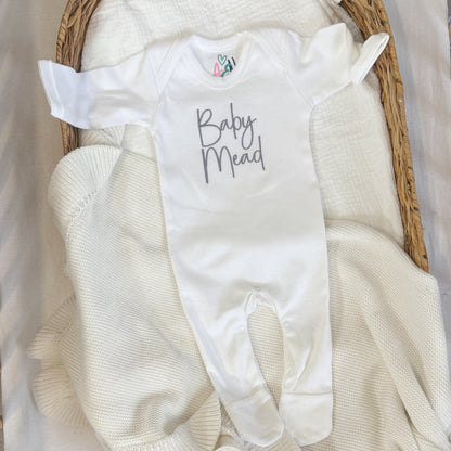 White baby sleepsuit with script name, short sleeves, and snap-fastening feet