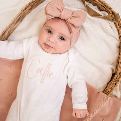 White long-sleeve baby sleepsuit with script 'Caitie' on chest