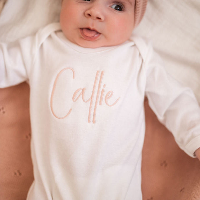 White long-sleeve baby sleepsuit with script 'Caitie' chest detail