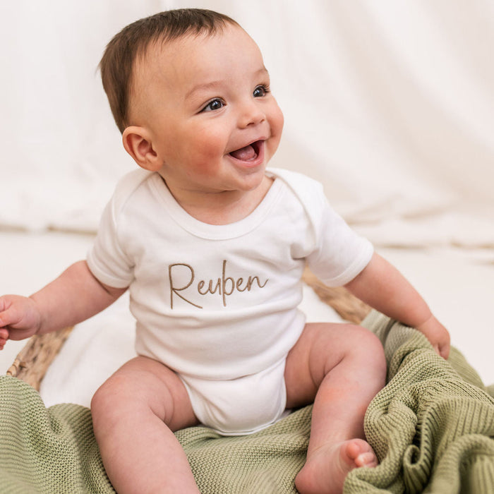 Personalised script baby vest with brown Reuben text on white fabric