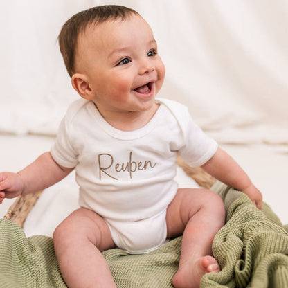 Personalised script baby vest with brown Reuben text on white fabric