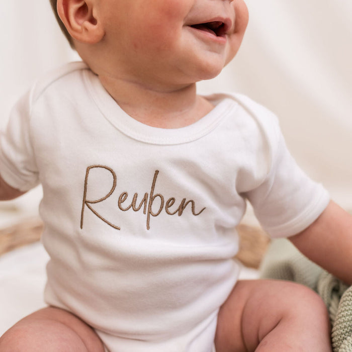 Personalised script baby vest, close-up of brown Reuben print on white