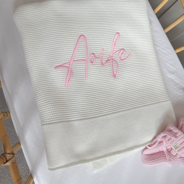 Close-up of white baby blanket with pink “Arfie” name embroidery and straight hem