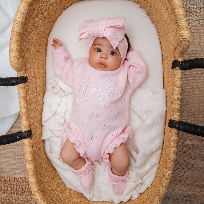 Pink knitted baby romper with 'Wolff' embroidery, long sleeves, and ruffle-trim legs