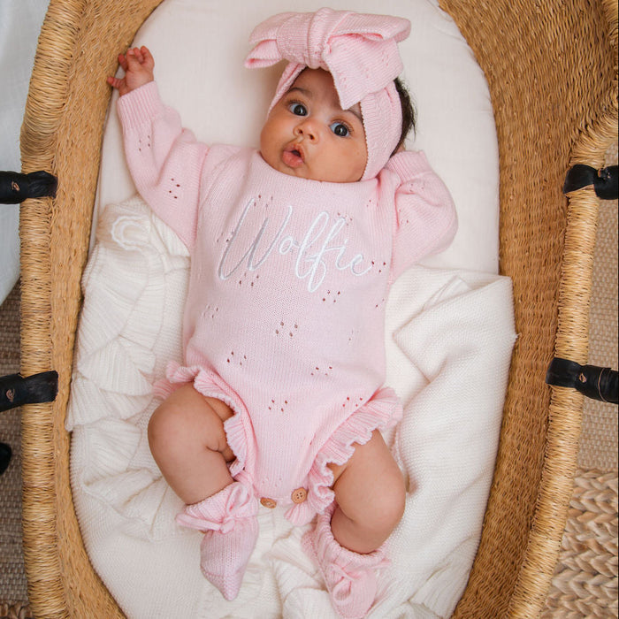 Pink pointelle romper on baby with 'Wolff' embroidery, bow-cuffed sleeves, ruffled legs