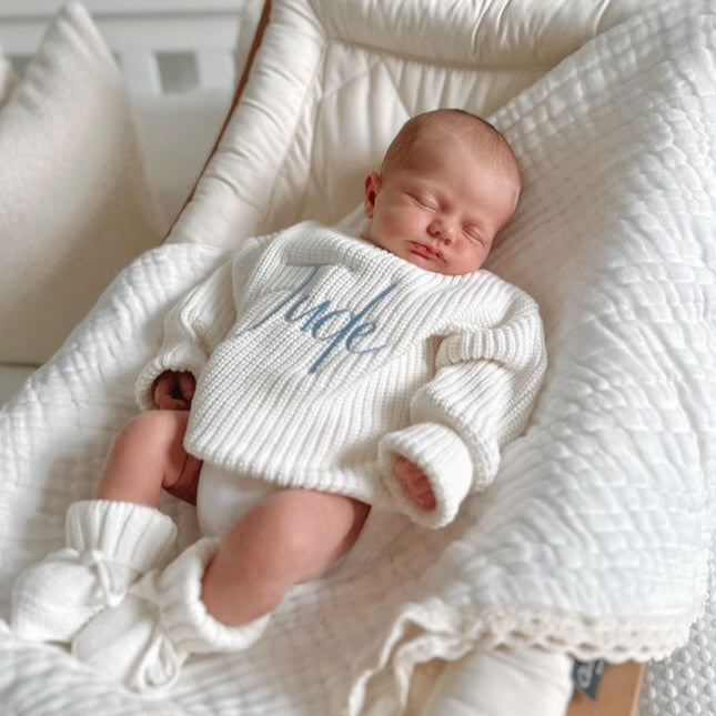 White chunky knitted baby jumper with blue script name and full long-sleeve styling
