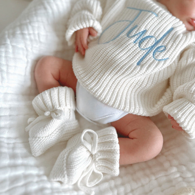 White chunky knitted baby jumper with ribbed cuffs and blue script name detail