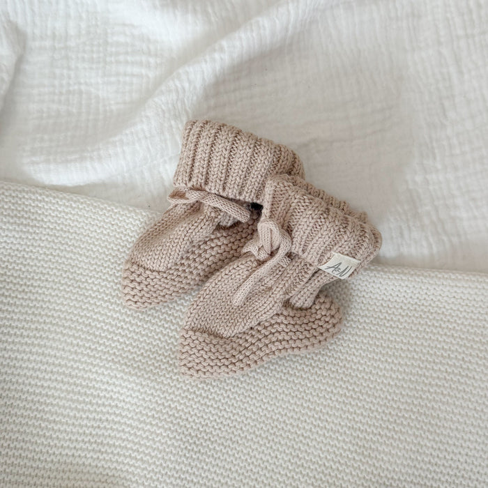 Beige knitted baby booties, side view with tied bow and folded cuff