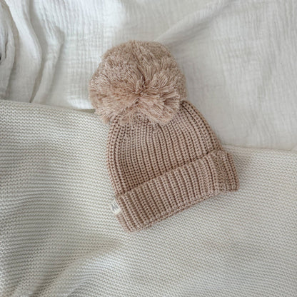 Beige knitted baby beanie with large pom-pom and ribbed brim