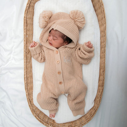 Beige knit romper with button placket and hood, topped with two pom pom beanie