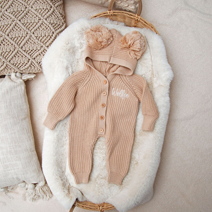 Beige knitted romper with long sleeves and button front, paired with pom pom beanie hat