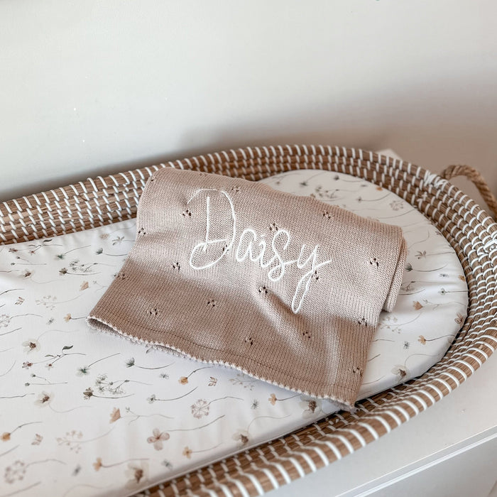 Beige personalized baby knit blanket with cursive embroidery, folded in a tray