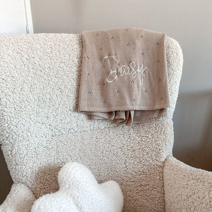 Beige pointelle baby knit blanket with embroidered name on textured fabric