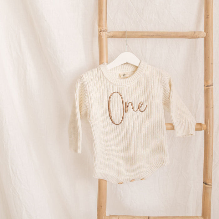 Cream knitted romper, 'One' embroidery at center, long sleeves, crew neckline