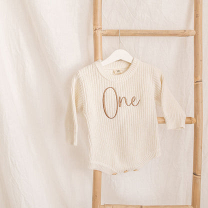 Cream knitted romper, 'One' embroidery at center, long sleeves, crew neckline