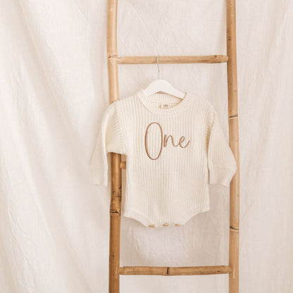 Knitted romper on hanger, cream knit with brown 'One' embroidery, long sleeves