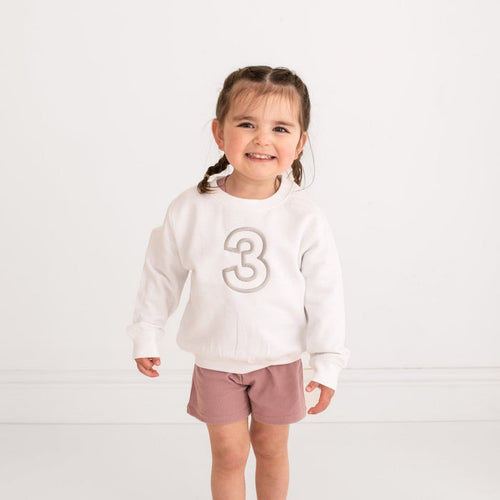 White crewneck sweater with embroidered '3' on front, long sleeves