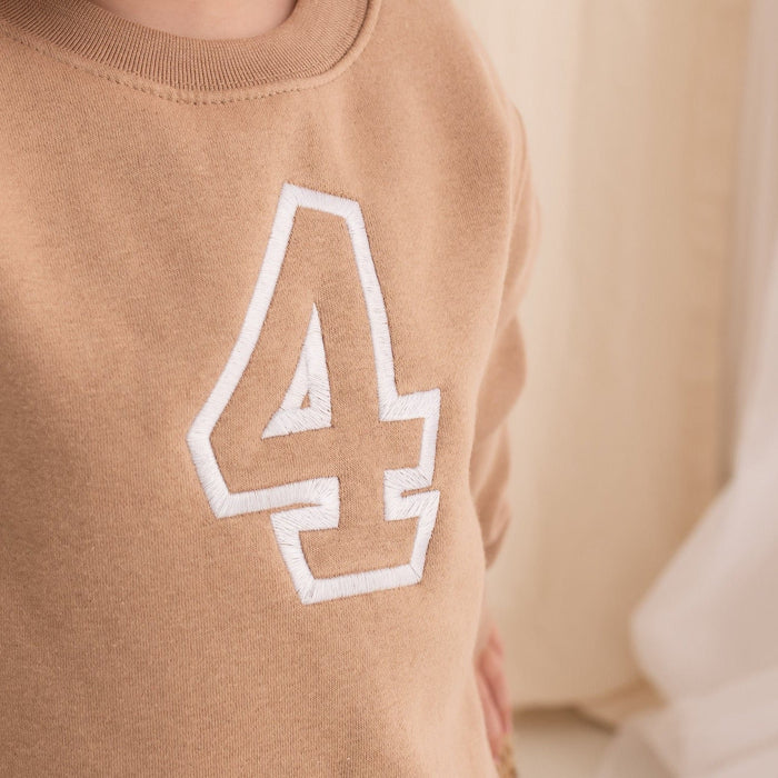 Tan sweater close-up with white-outlined embroidered '4' patch