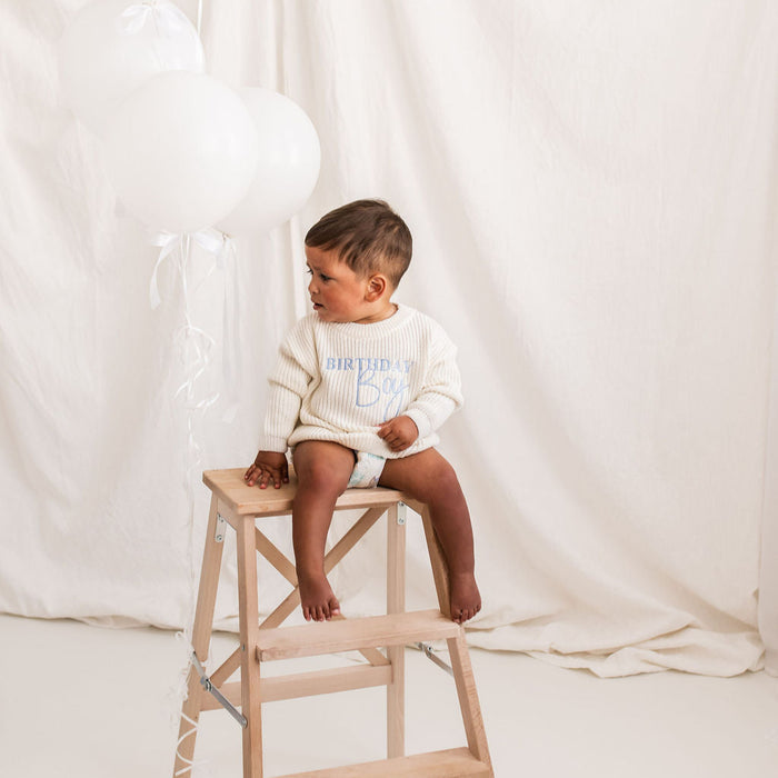 White knitted jumper with blue Birthday Boy print, on child seated