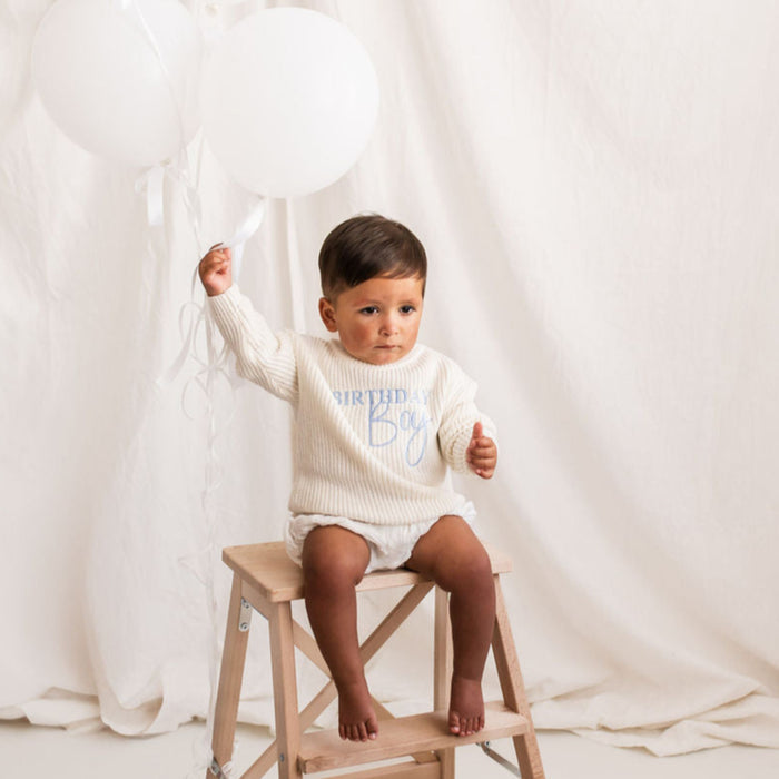 White knitted jumper with blue Birthday Boy print, on child holding pose