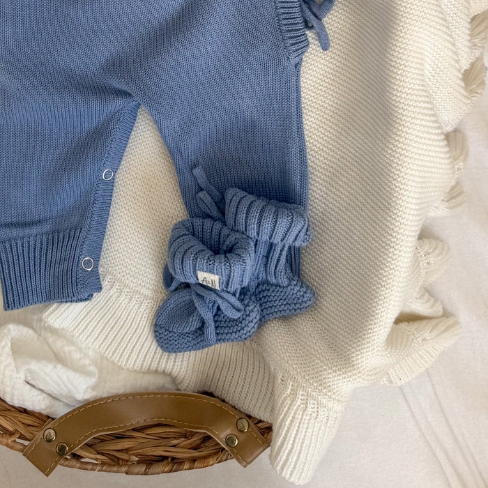 Blue knitted baby booties with bow and ribbed knit cuff near onesie