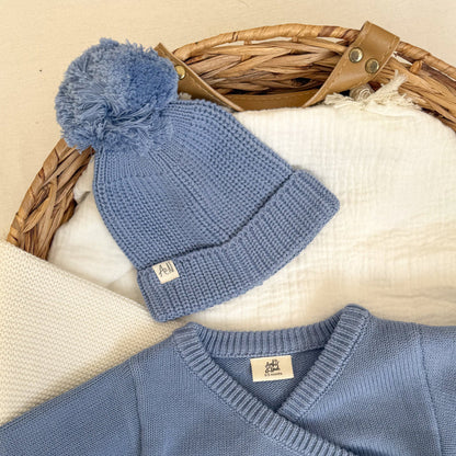 Blue knitted baby hat with pom-pom and ribbed brim, small tag
