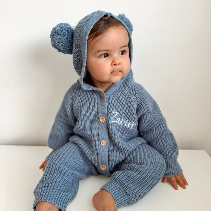 Blue knit romper with hood and pom-poms, button front, and 'Ziver' name embroidery