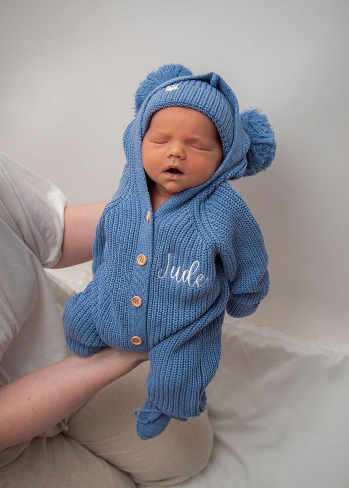 Blue knitted hooded romper with pom-pom details and “Jude” embroidery, button front