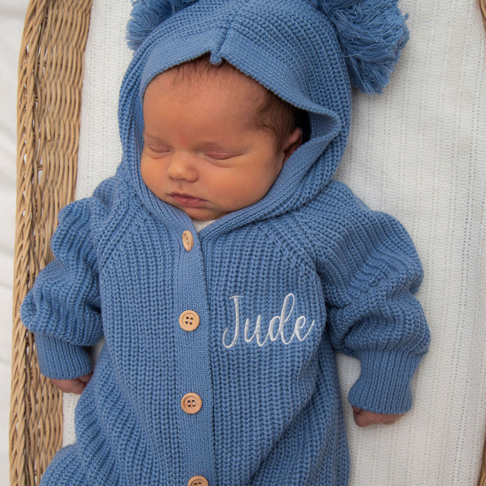 Blue knitted hooded romper with “Jude” embroidery and button front, pom-pom hat