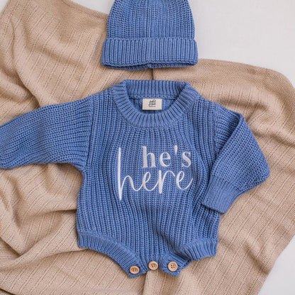 Blue knitted romper with white embroidered text “he’s her”, round neckline