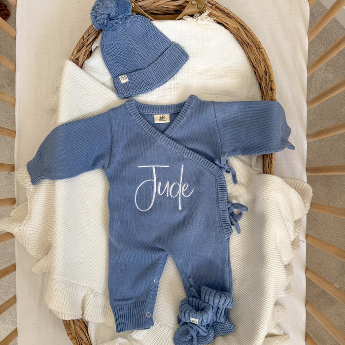 Blue knit romper with 'Jude' script, envelope-style crossover and tied shoulder bows.