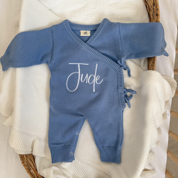 Blue knit romper with 'Jude' script, long sleeves and buttoned legs.