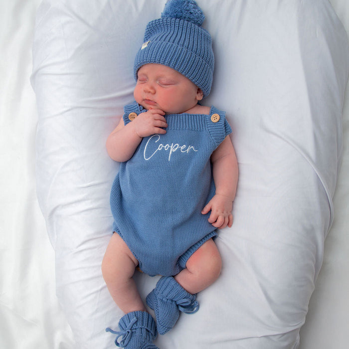 Blue knit personalised romper with button shoulders and matching blue beanie, close-up