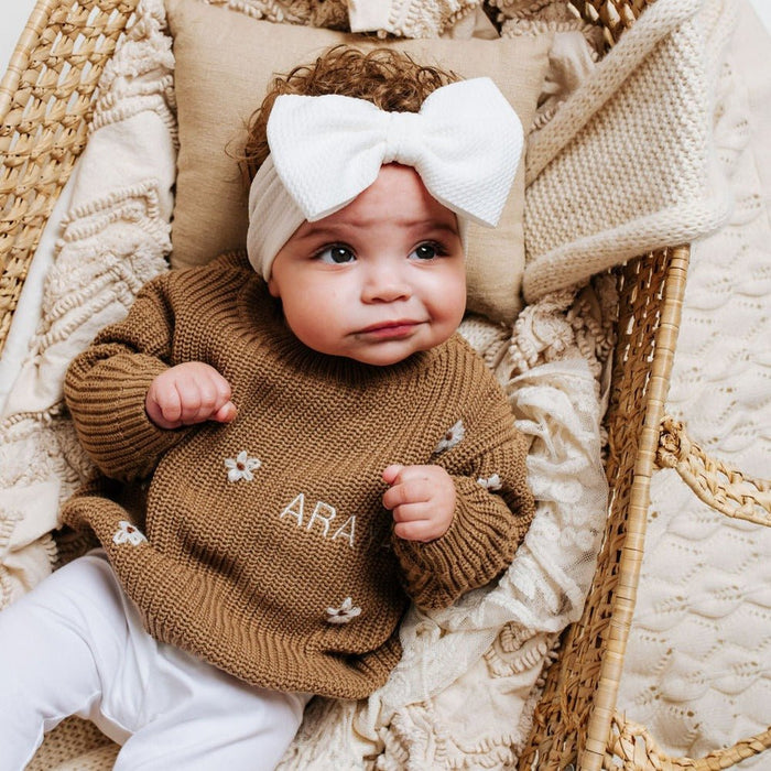 Brown knitted baby jumper with white floral appliqués and partial name embroidery