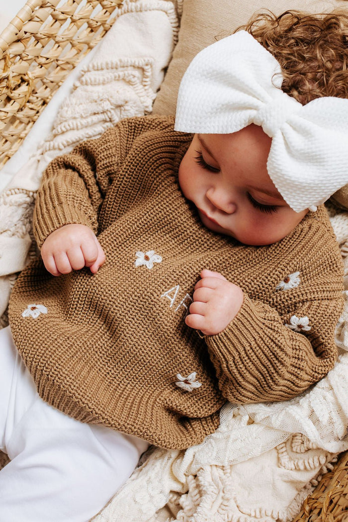 Brown knitted baby jumper with white floral appliqués, folded cuffs on baby