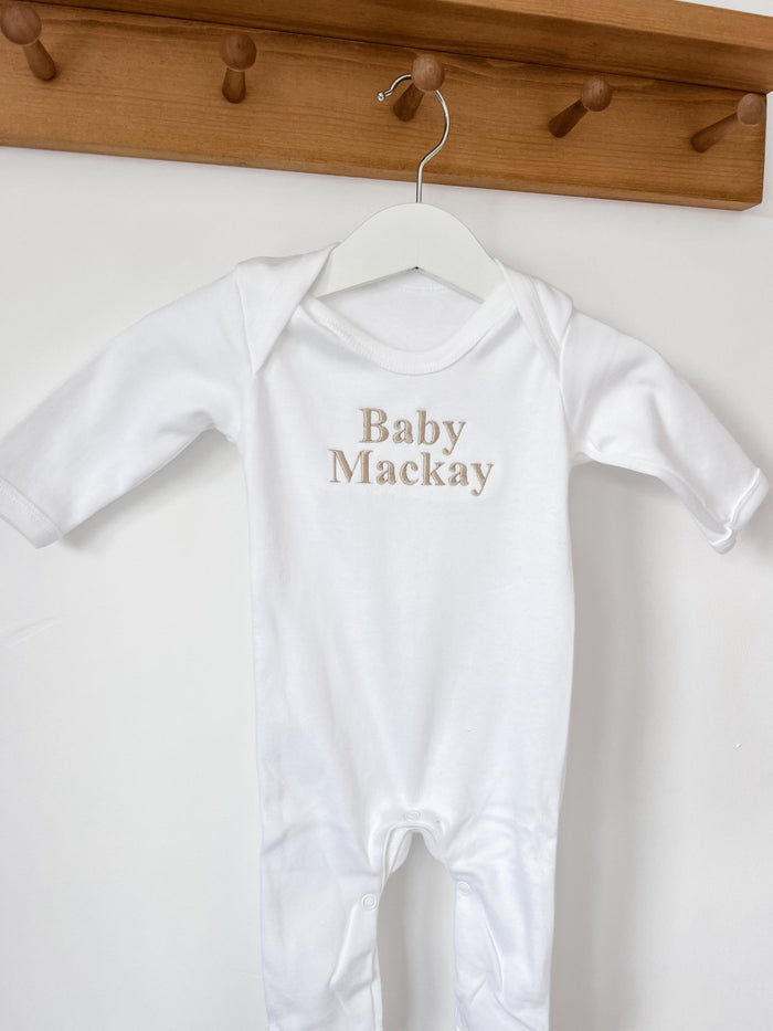 White baby sleepsuit with long sleeves, 'Baby Mackay' logo on chest